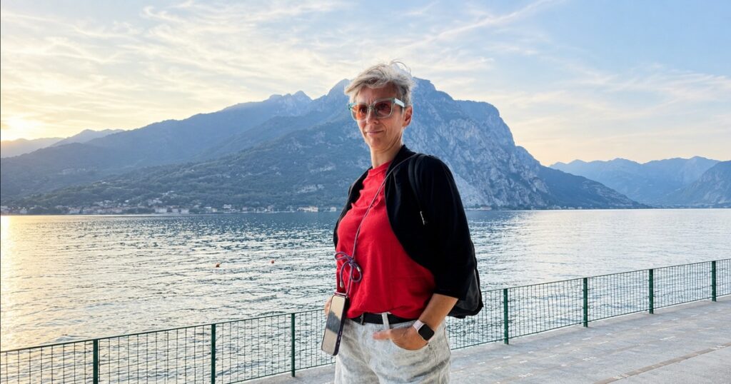 Immagine elaborata con l'AI: Federica Perini sul lungolago, maglietta rossa e felpa nera, con il lago e la montagna alle spalle